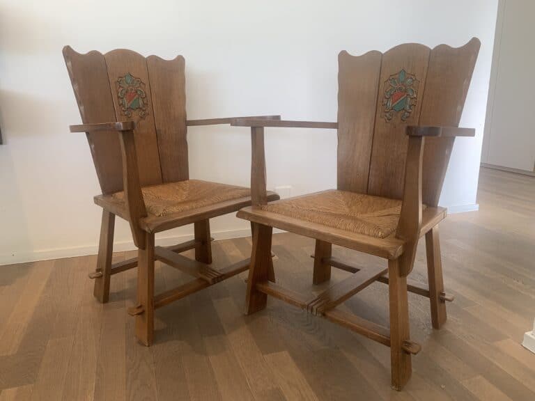 Twee vintage houten fauteuils met hoge rugleuningen en decoratieve bloemeninlegsels, naast elkaar op een lichte houten vloer tegen een witte muur.