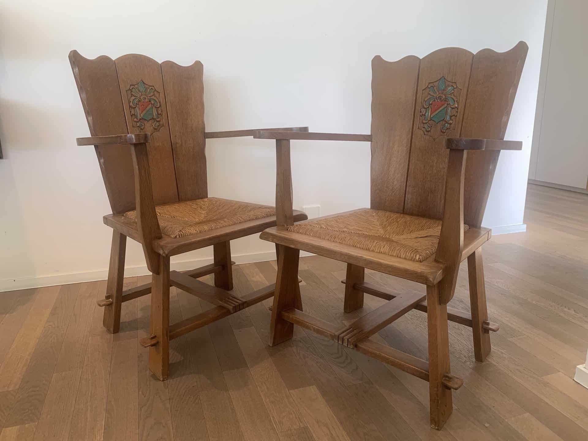 Twee vintage houten fauteuils met hoge rugleuningen en decoratieve bloemeninlegsels, naast elkaar op een lichte houten vloer tegen een witte muur.