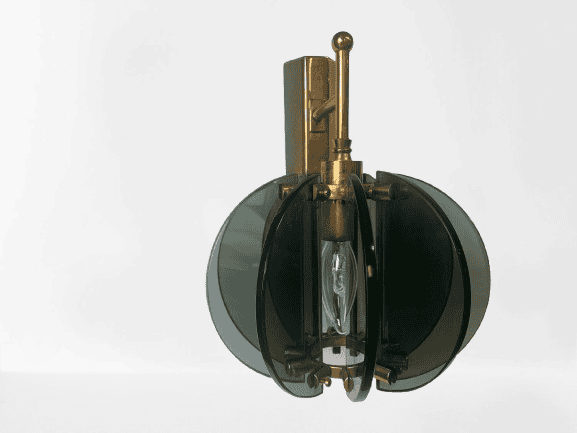 Een vintage wandlamp met in het midden een zichtbare gloeilamp, omgeven door vier donkergroene glaspanelen en messing elementen, tegen een effen witte achtergrond.