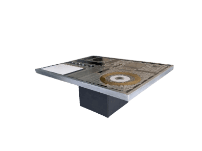 Een rechthoekige tafel met een metalen bovenblad met patroon, waarop verschillende geometrische ontwerpen staan, waaronder een cirkelvormig motief en vierkante tegels. De tafel wordt ondersteund door een zwart onderstel in het midden.