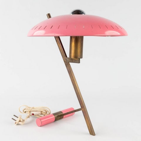 Een vintage tafellamp met een roze, koepelvormige kap, een schuine messing voet en een bijpassende roze cilindrische schakelaar. De lamp heeft een retro design en een wit snoer met stekker.