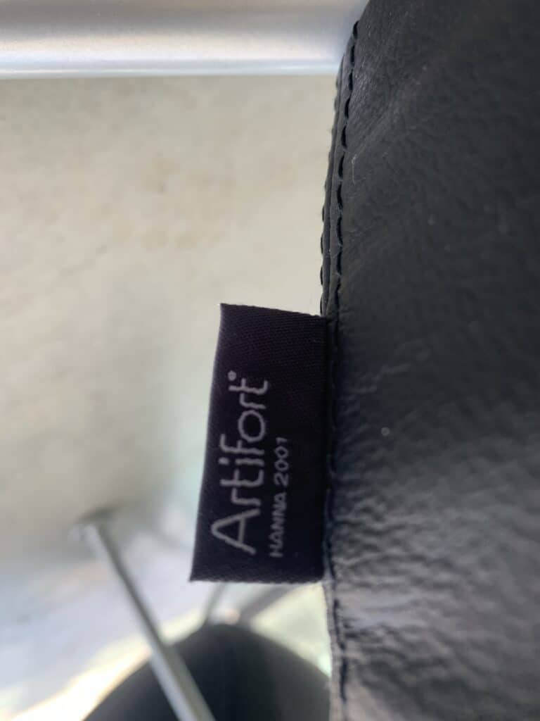 Een close-up van een zwart stoffen label genaaid op zwarte leren bekleding. Op het label staat 