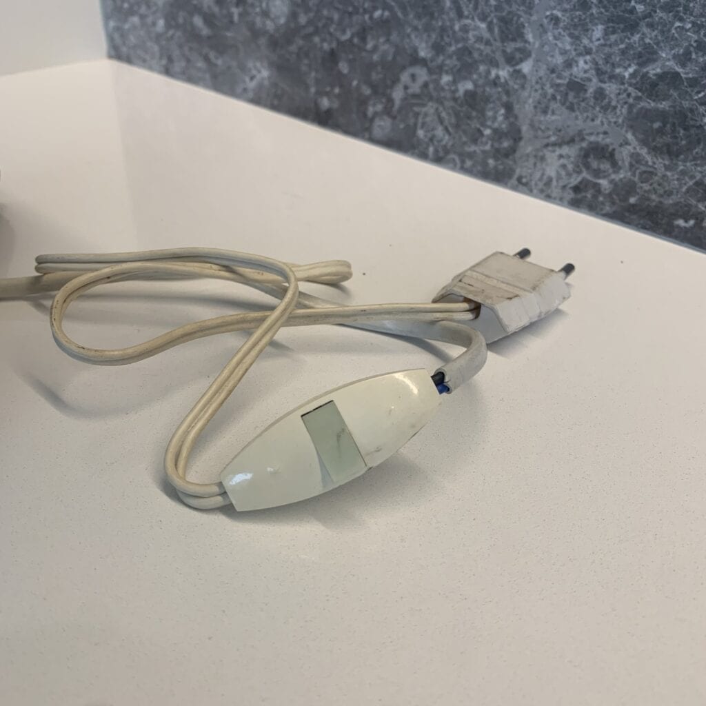 Een wit elektrisch snoer met een schakelaar en een Europese stekker bedekt met wit tape, rustend op een wit oppervlak naast een grijze marmerachtergrond.