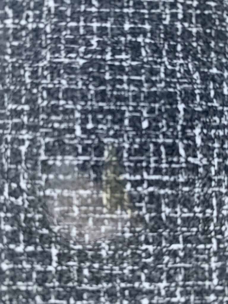 Close-upfoto van een zwart-wit stoffenpatroon met een rechthoekige vlek waarop wat lichte gelige markeringen en een lichte lichtreflectie te zien zijn.