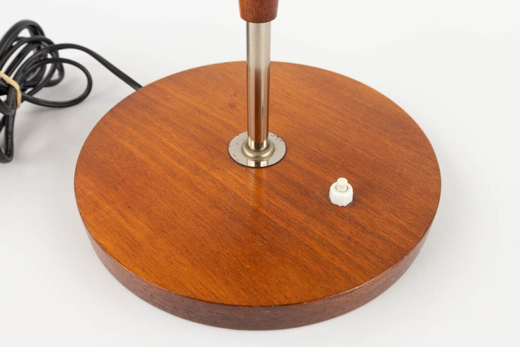 Een close-up van een lampenvoet van gepolijst hout met een metalen steel, een witte plastic knop en een zwart snoer op een witte achtergrond.