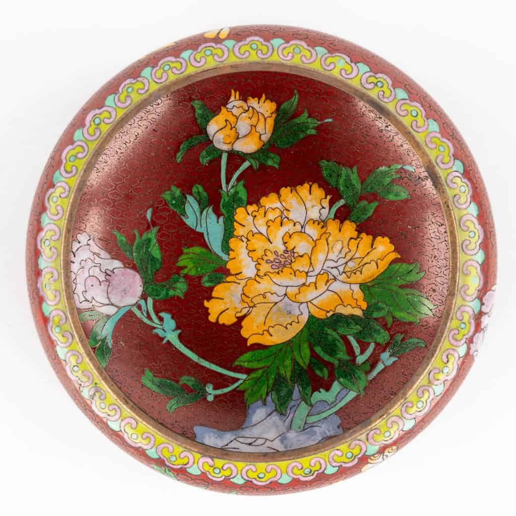 Een rond, rood decoratief bord met een geschilderd dessin van gele en witte pioenrozen met groene bladeren, omzoomd met een geel en wit sierlijk patroon.