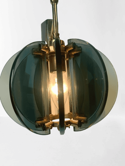 Een moderne hanglamp met een zichtbare gloeilamp in het midden, omgeven door ronde, getinte glaspanelen en gouden accenten, hangt tegen een eenvoudige witte achtergrond.