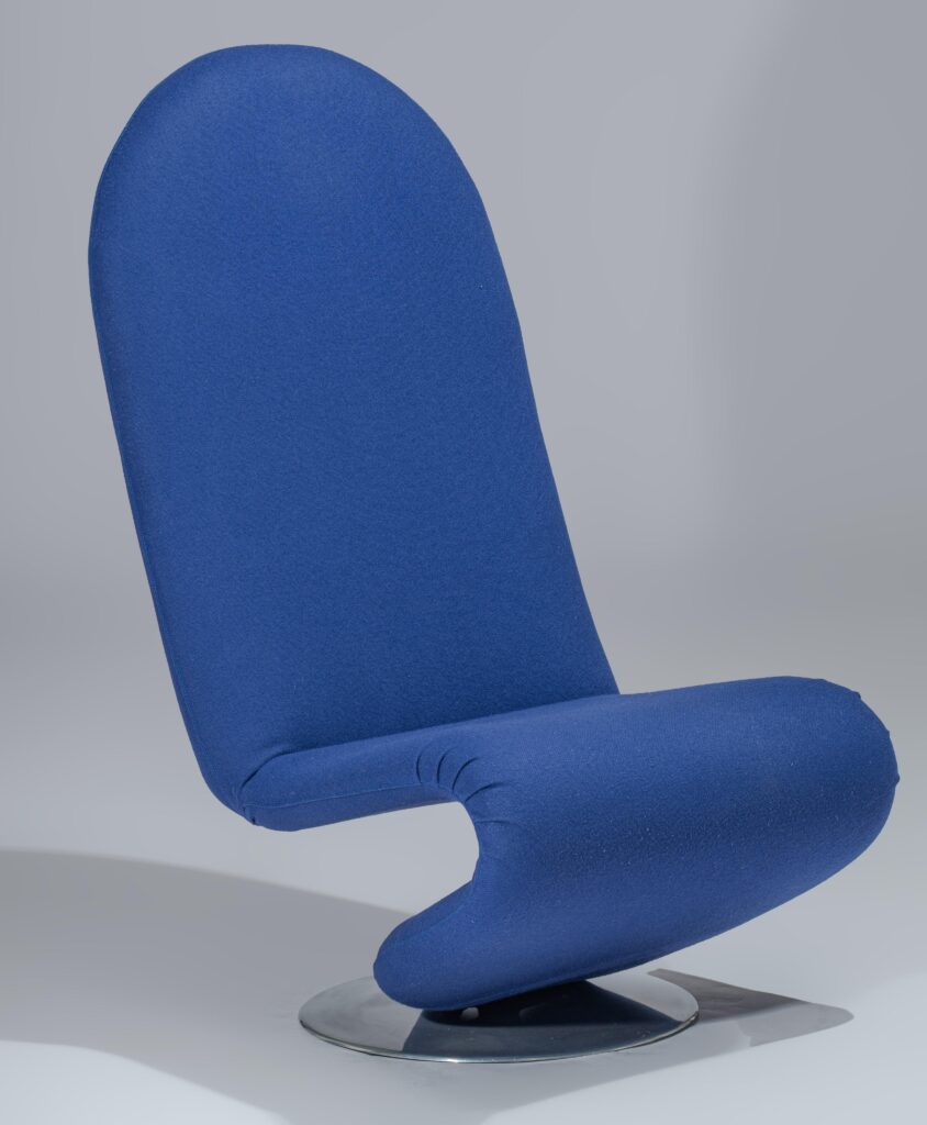 Een moderne, blauw gestoffeerde stoel met een hoge, ronde rugleuning en een gebogen zitting op een rond metalen onderstel, tegen een effen grijze achtergrond.