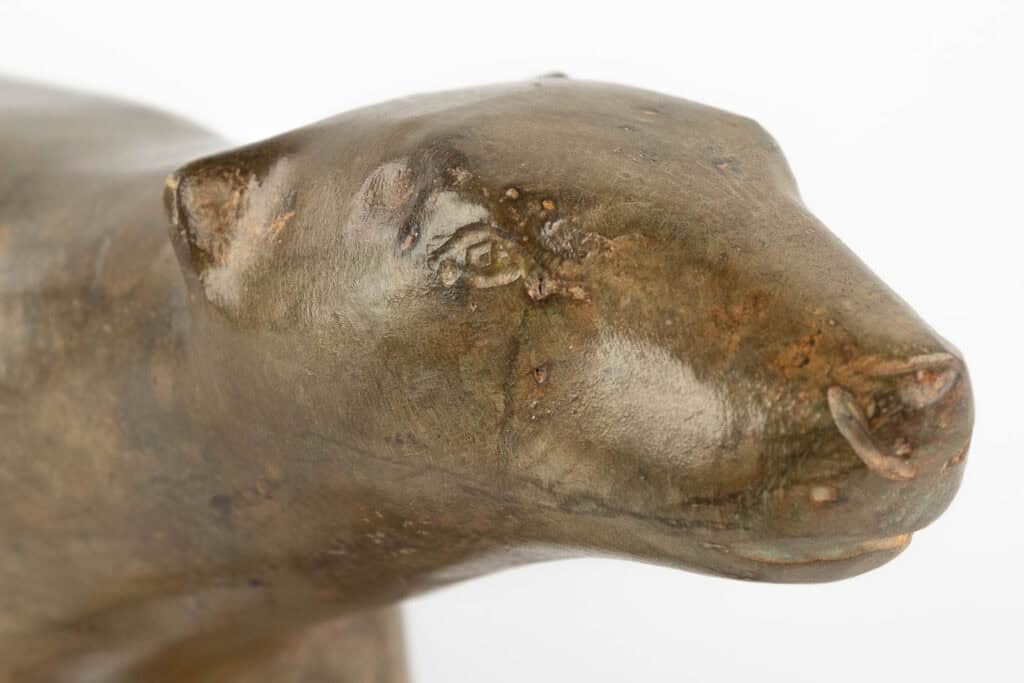 Close-up van een glad, bruingroen dierenbeeld, waarschijnlijk een beer, met zichtbare textuur en ronde gelaatstrekken, tegen een effen witte achtergrond.