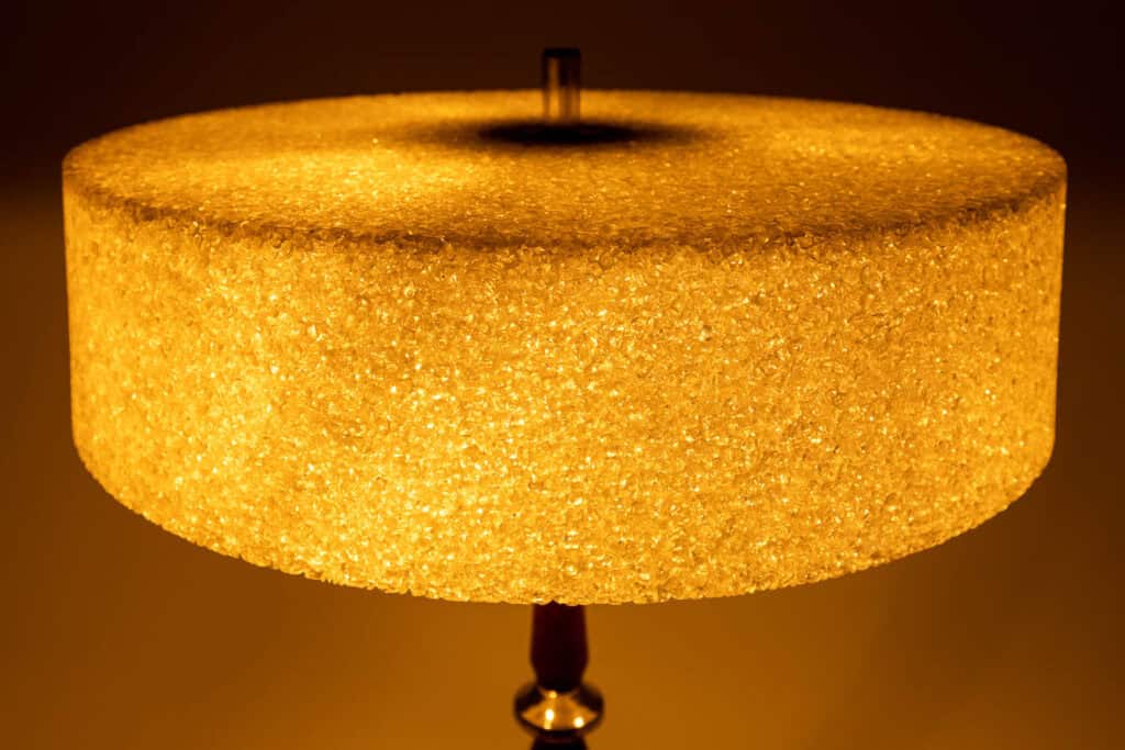 Een close-up van een gloeiende, gestructureerde cilindrische lampenkap van doorschijnend materiaal, die een warm gouden licht uitstraalt met zachte schaduwen op de achtergrond.