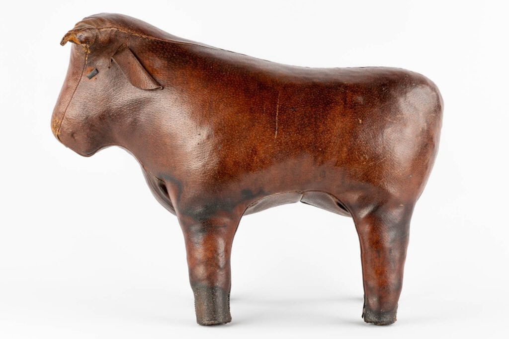 Een bruin leren sculptuur van een staande stier, afgebeeld in profiel tegen een witte achtergrond. De stier heeft stevige poten, een rond lichaam en minimale gelaatstrekken.