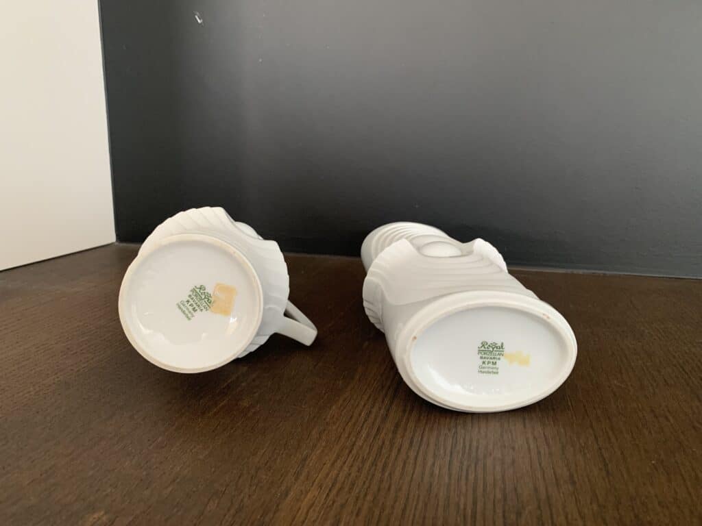 Twee witte keramische mokken met een Star Wars Stormtrooper-helm liggen op hun zij op een donker houten oppervlak, met het groene Royal Selangor-logo en labels op de onderkant.