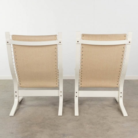 Twee moderne stoelen met een wit houten frame en een beige stoffen rugleuning, van achteren gezien en naast elkaar geplaatst op een lichtgrijze vloer en tegen een effen witte muur.