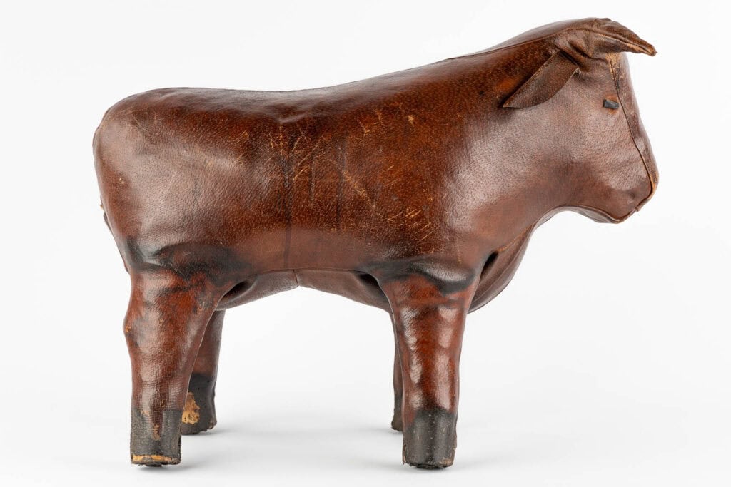 Een bruin leren sculptuur van een stier op vier poten, van opzij gezien tegen een witte achtergrond. Het beeld heeft zichtbare textuur en lichte slijtage, met details op de oren en poten.