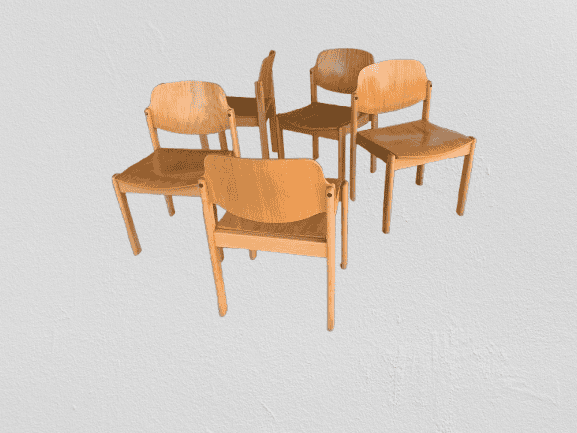 Vier lichte houten stoelen met gebogen rugleuningen en vierkante zittingen zijn in een losse, trapsgewijs geplaatste groep geplaatst tegen een effen, lichtgekleurde, gestructureerde achtergrond.