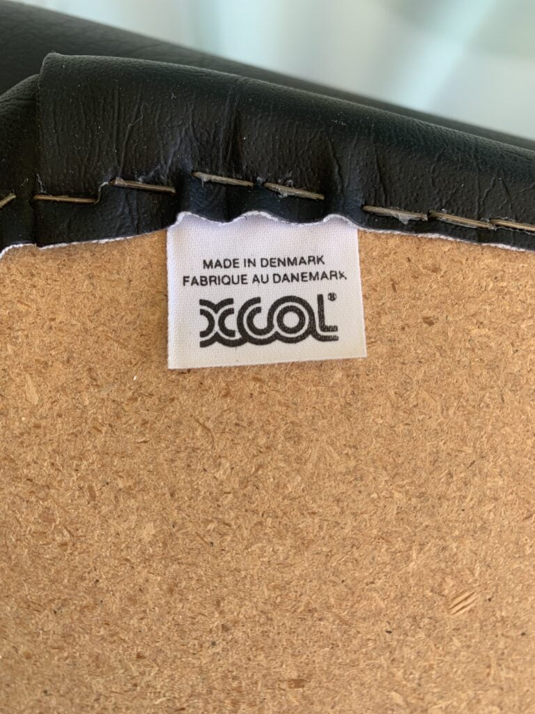 Een close-up van een wit label genaaid op een meubelstuk. Op het label staat in zwarte letters 