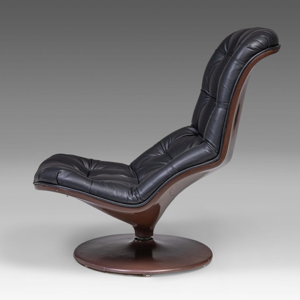 Een moderne, zwarte leren loungestoel met gecapitonneerde kussens en een glad, gebogen design. De stoel rust op een ronde, bruine voet, tegen een effen grijze achtergrond.