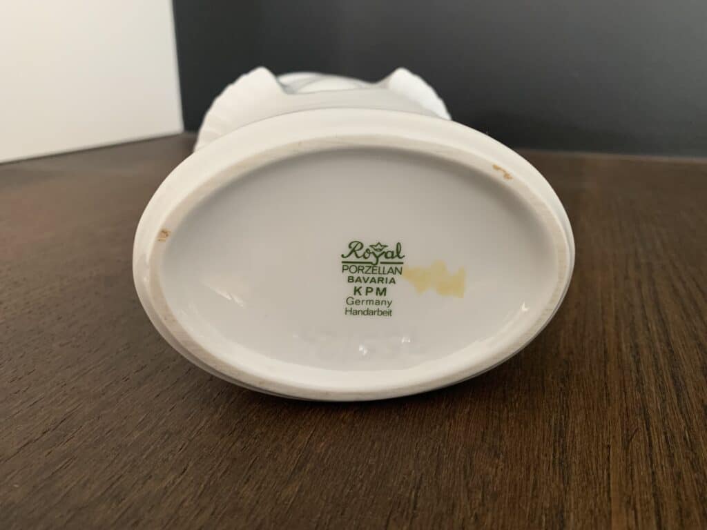 De voet van een porseleinen beeldje is afgebeeld, met het makersmerk: 