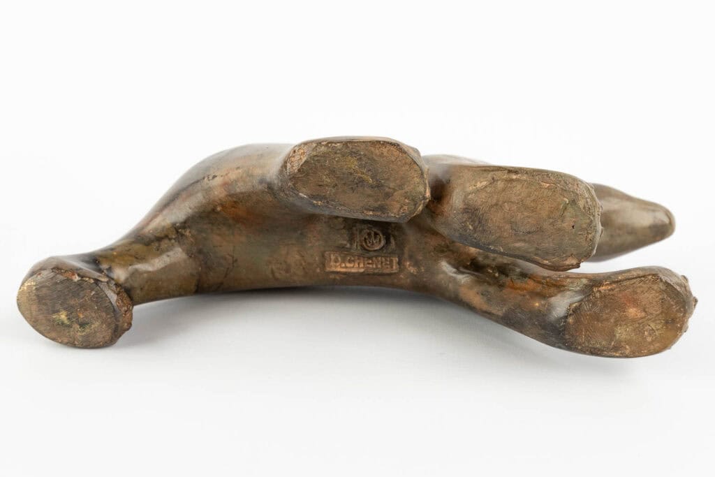 Bronzen beeld van een menselijke hand die met de handpalm naar beneden op een witte achtergrond ligt, met de handtekening van de kunstenaar en het copyrightsymbool op de onderkant van de handpalm.