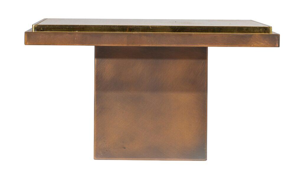Een moderne rechthoekige tafel met een dik, plat blad en een brede, massieve voet, beide gemaakt van gepolijst bruin metaal. Het tafelblad heeft een licht opstaande, lichter gekleurde rand. De achtergrond is wit.