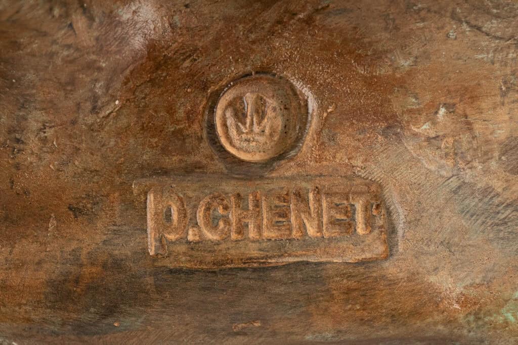 Een close-up van een bronzen oppervlak met een gestempeld merkteken met een kroon erboven, de initialen 