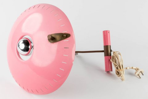 Een vintage roze wandlamp met een ronde kap, een chromen bol en een roze cilindervormige bevestiging. Aan de zijkant is een snoer met stekker zichtbaar, dit alles tegen een witte achtergrond.