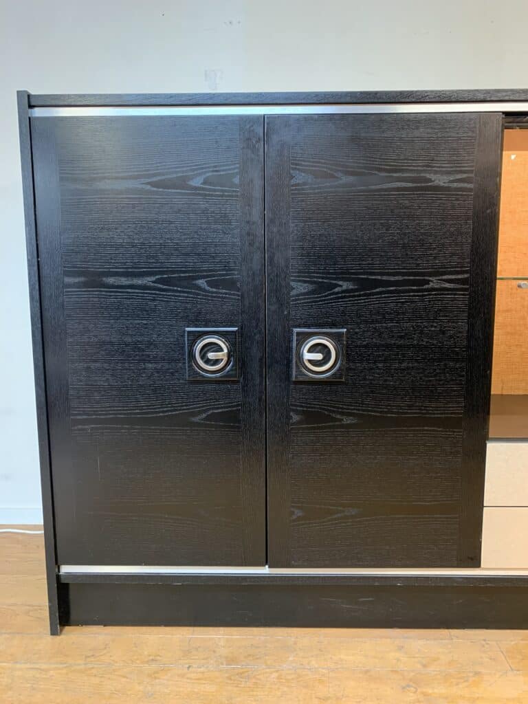 Een paar schuifdeuren van donker hout met ronde metalen handgrepen, in een zwart houten frame tegen een lichtgekleurde muur, op een houten vloer.