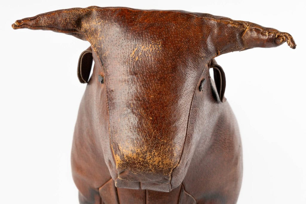 Een close-up van een vintage, bruinleren dierensculptuur dat lijkt op een stier met prominente hoorns, een gestructureerd oppervlak en zichtbare slijtage op de neus. De achtergrond is wit.
