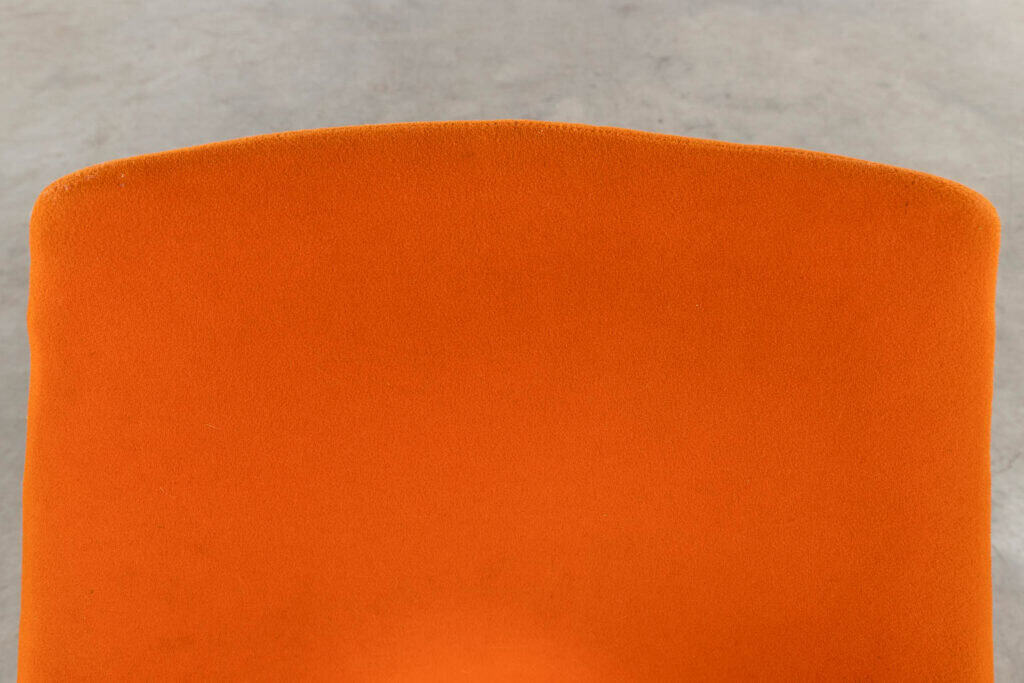 Close-up van de rugleuning van een oranje gestoffeerde stoel, met een wazige grijze vloer op de achtergrond.