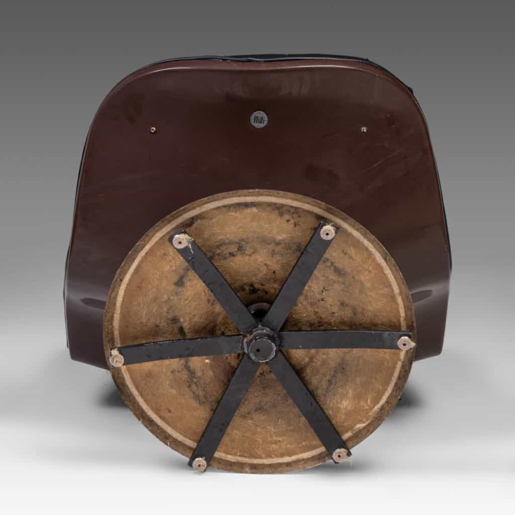 Een bruine rolstoel, van voren gezien, met een groot, rond houten voorwiel met zes zwarte metalen spaken en bouten die het wiel vastzetten. De achtergrond is een effen grijze gradiënt.
