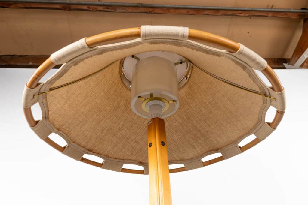 Close-up van een beige stoffen parasol met een houten stok en een rond houten frame, afgebeeld tegen een witte achtergrond en een gedeeltelijk plafond.