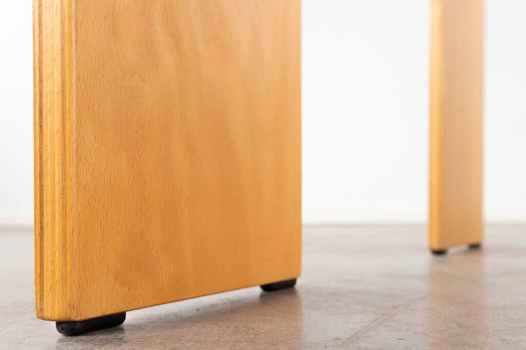 Close-up van het onderste deel van twee lichte houten tafel- of meubelpoten met kleine zwarte voetjes, staand op een gladde, lichte vloer tegen een witte achtergrond.