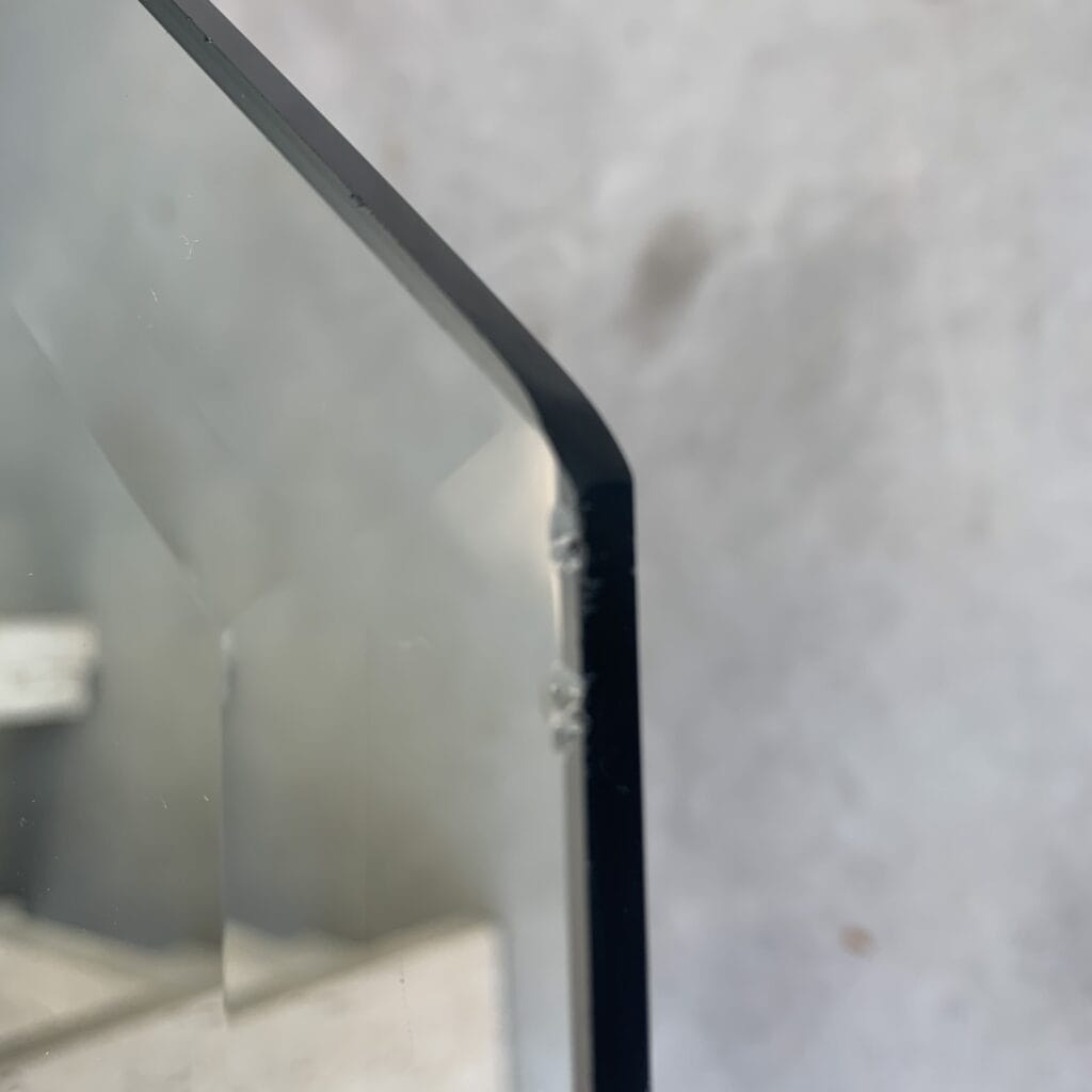 Close-up van de hoek van een glaspaneel met een zichtbare kleine chip of scheur aan de rand. De achtergrond is onscherp en lijkt grijs en neutraal.